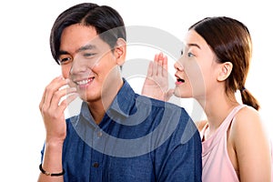 Studio shot of young happy Asian couple smiling with woman whisp