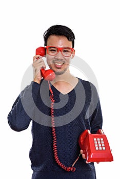 Studio shot of young happy Asian man smiling while talking on ol