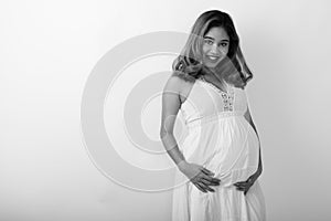 Studio shot of young happy Asian pregnant woman smiling against white background