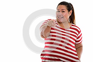 Studio shot of young happy fat Asian woman smiling while pointin