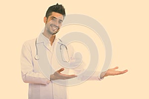Studio shot of young happy Persian man doctor smiling while showing something