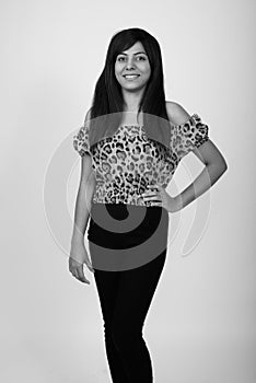 Studio shot of young happy Persian woman smiling while standing and posing against gray background