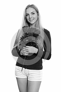 Studio shot of young happy teenage girl smiling while holding roses ready for Valentine`s day