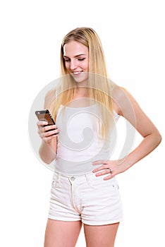 Studio shot of young happy teenage girl smiling while using mobi