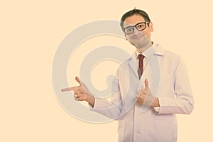 Studio shot of young man doctor pointing to the side and giving thumb up