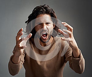Youre making my blood boil. Studio shot of a young man screaming in anger against a gray background.