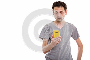 Studio shot of young man using mobile phone while looking shocke