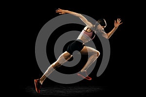 Studio shot of young muscular woman running isolated on black background. Sport, track-and-field athletics, competition