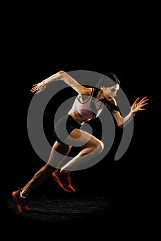 Studio shot of young muscular woman running isolated on black background. Sport, track-and-field athletics, competition