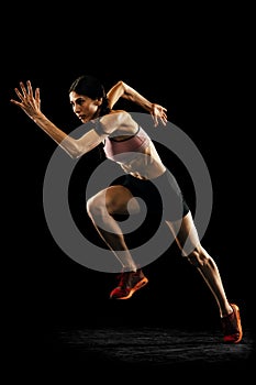 Studio shot of young muscular woman running isolated on black background. Sport, track-and-field athletics, competition