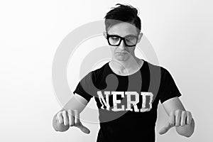 Studio shot of young nerd man looking sad and giving thumbs down while wearing eyeglasses against white background