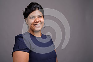 Young overweight beautiful Indian woman against gray background