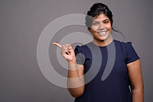 Young overweight beautiful Indian woman against gray background