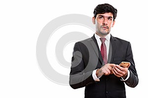 Studio shot of young Persian businessman using mobile phone whil
