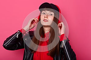 Studio shot of young pretty teenager girl wearing red hoody and leather jacket, looking directly at camera with pleasant facial