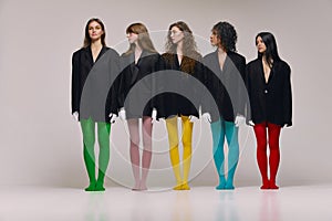 Studio shot of young stylish beautiful fashion models in black jackets and multi colored tights posing over grey