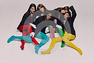 Studio shot of young stylish beautiful fashion models in black jackets and multi colored tights posing over grey