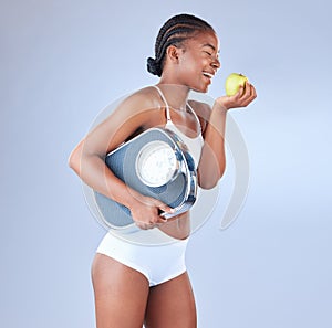 Fall in love with taking care of your health. Studio shot of a young woman eating an apple and holding weighing scale