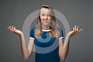 Studio shot of a young woman shrugging shoulders looking at the camera being at loss. Concept of doubt and uncertainty