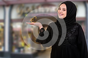 Studio shot of young woman wearing traditional arabic clothing. she`s holding pound symbol in hand.