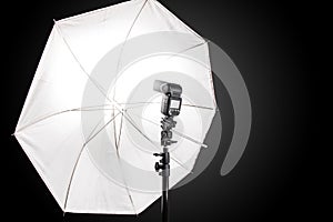 Studio stand with speedlight photo flash and white umbrella reflector