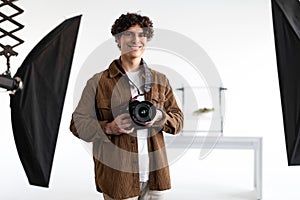 Studio stories. Positive guy holding digital camera, professional photographer enjoying his job at photostudio