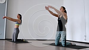 In the studio, two girls are engaged in pilates. Standing on their knees deviate back training the front of the thigh