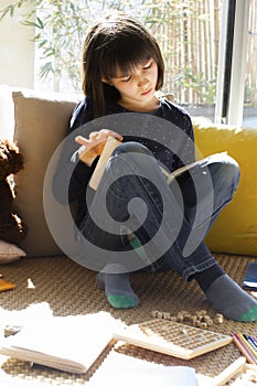 Studious child reading with teddy bear and board games around