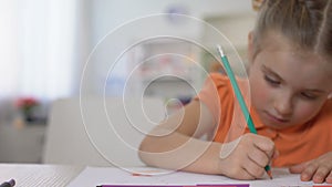 Studious little girl writing with pencil at home table, childhood education