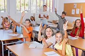 Studious preteen pupils raising hands to answer in class