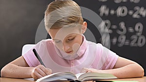 Studious pupil writing test work, school lessons, math equation on blackboard