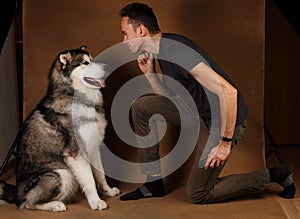 Studo shot of a man and alaskan malamute dog stitting on brown blackground