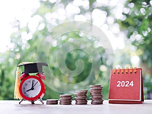 Study goals, 2024 Desk calendar, Red alarm with graduation hat and stack of coins. The concept of saving money for education,