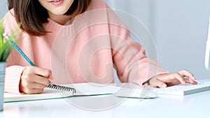 Study online class, Woman hand writing on notebook while tying computer keyboard, Adult female student learning online course,