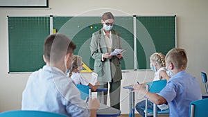 Studying in schools after quarantine, teacher handing out leaflets with assignment to kids during lesson, portrait of