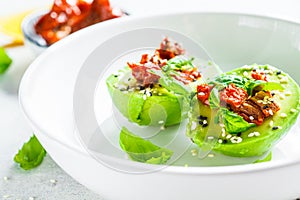 Stuffed avocado halves with sun-dried tomatoes and basil on white plate. Healthy vegan food concept