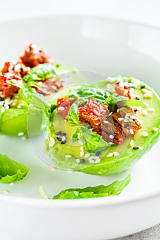 Stuffed avocado halves with sun-dried tomatoes and basil on white plate. Healthy vegan food concept