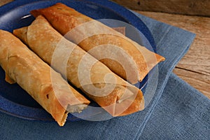 Stuffed filo or yufka dough rolls with a spicy meat filling on a blue plate on a rustic wood, selected focus