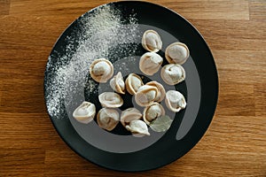 Stuffed homemade dumplings on a dark plate with flour on wooden table. Russian pelmeni