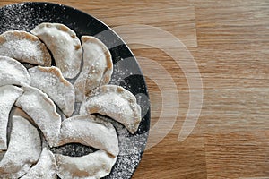 Stuffed homemade dumplings on a dark plate with flour on wooden table. Ukrainian vareniki