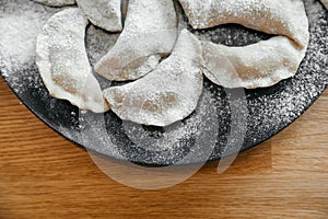 Stuffed homemade dumplings on a dark plate with flour on wooden table. Ukrainian vareniki