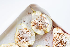 Stuffed pears dessert in white baking dish. Halves of pears with nuts, cinnamon and icing sugar. Dessert recipe