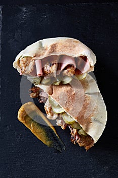 Stuffed pita bread with grilled vegetables and chiken chops on black stony background.