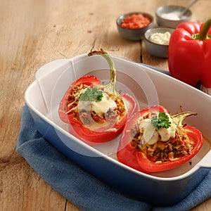 Stuffed red bell pepper baked with cheese in a blue casserole dish on a rustic wooden table