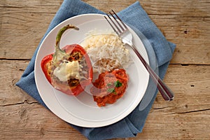 Stuffed red bell pepper baked with cheese gratin, rice and tomato sauce on a plate and a blue napkin, rustic wooden table, copy