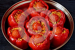 Stuffed red bell peppers with rice and vegetables in the baking dish on the black background close up