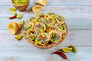 Stuffed tortilla cones with fajita on wicker basket with lime and guacamole