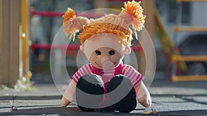 A stuffed toy doll sits on the ground on the playground. Close-up. The concept of adoption and lost children