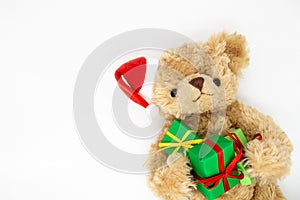 A stuffed toy Teddy bear in a red Santa Claus hat with a pompom on one ear, holding green gift boxes in its paws. White background
