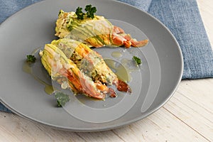 stuffed zucchini or courgette blossoms baked with parmesan cheese and parsley garnish on a blue gray plate